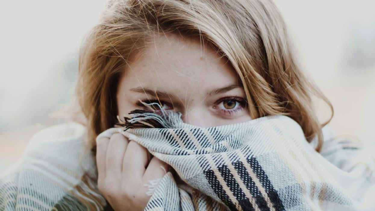 Woman cringing and covering her face with a scarf
