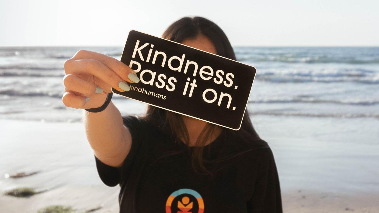 Woman holding sign that reads, "Kindness. Pass It On."