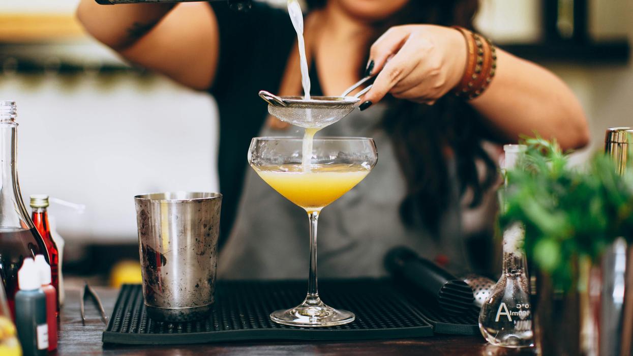 woman in black top and apron pouring cocktail in glass