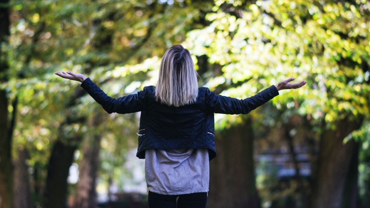 woman in longsleeves in front of trees making why gesture