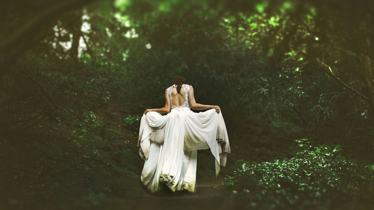 woman in white dress walking on pathway surrounded by trees