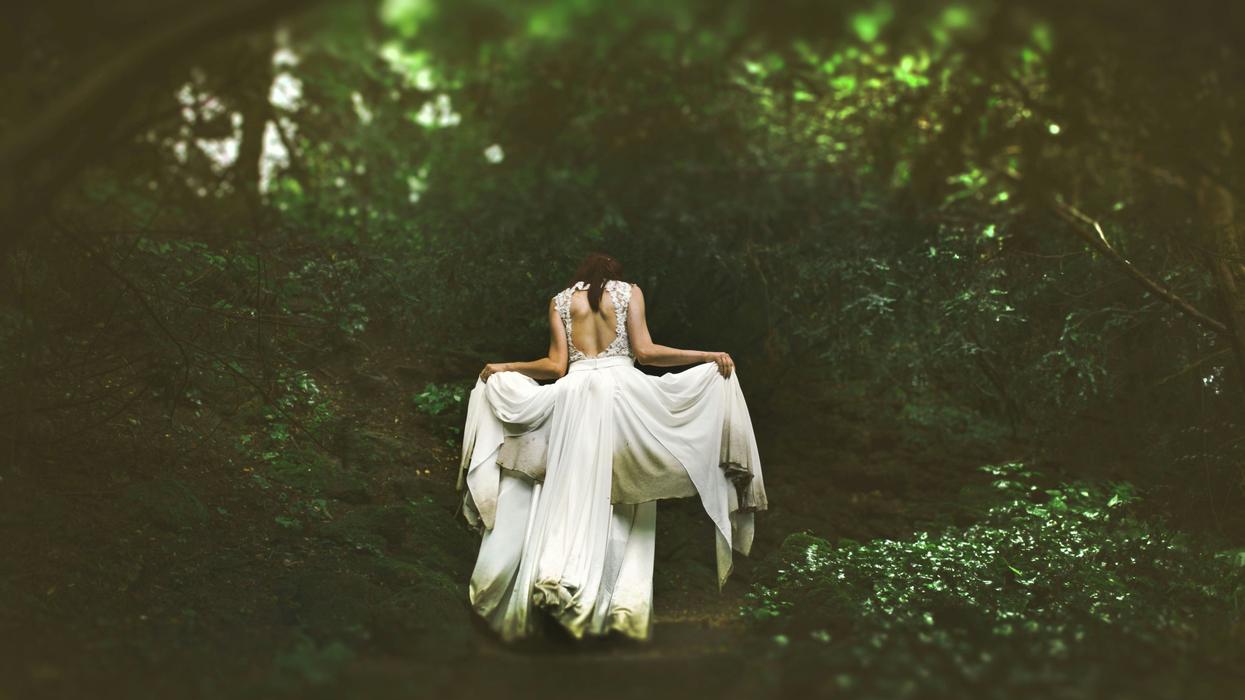 woman in white dress walking on pathway surrounded by trees