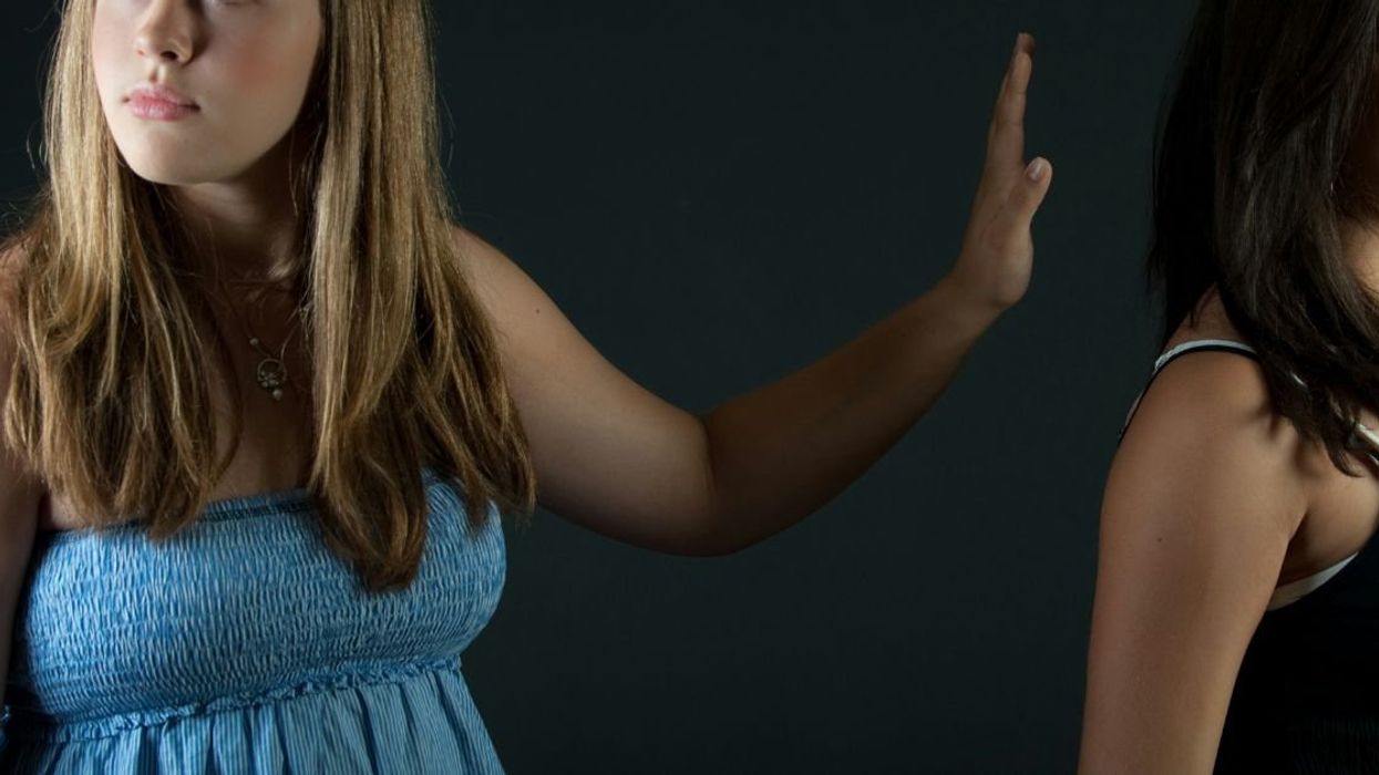 Woman putting up a "don't speak" hand gesture towards other woman