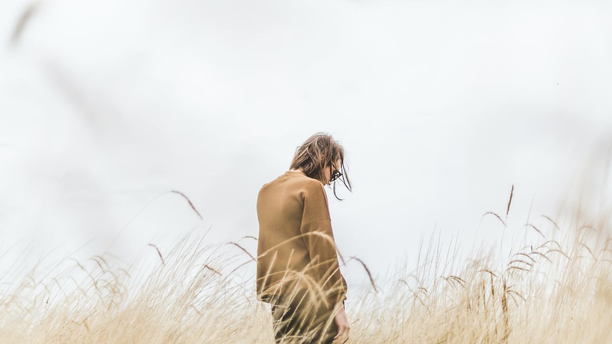 Woman walking through field looking sad.
