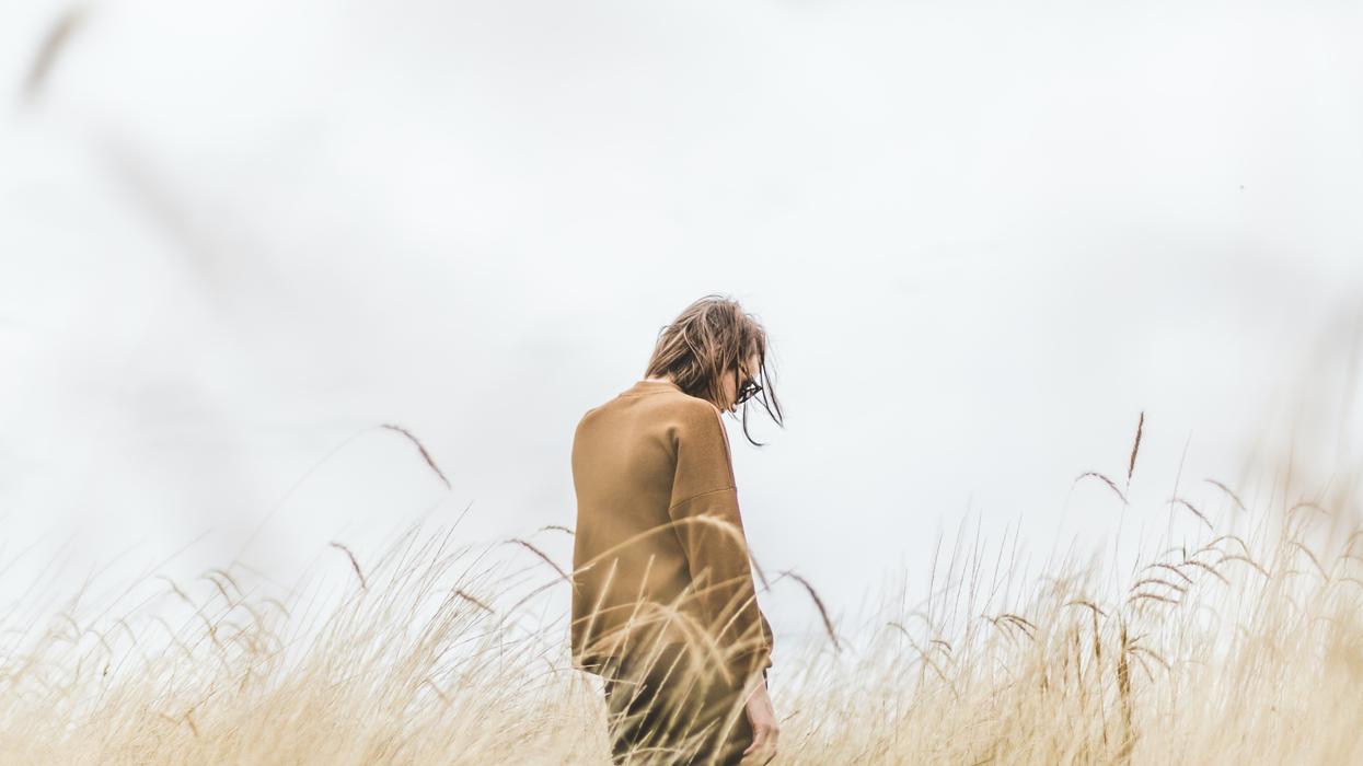 Woman walking through field looking sad.