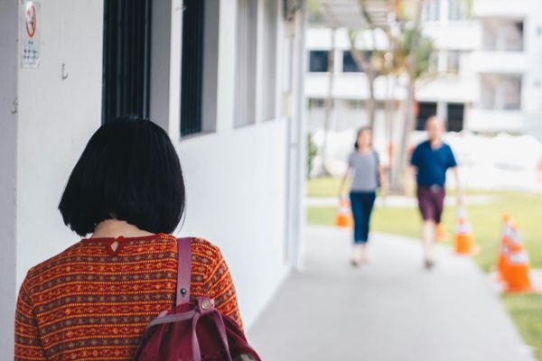 Woman walling with a bag over her shoulder and a couple walking towards her.
