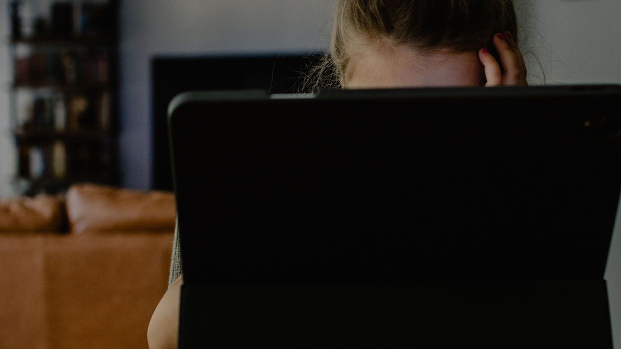 Woman with her head in her hands behind a laptop comuputer.